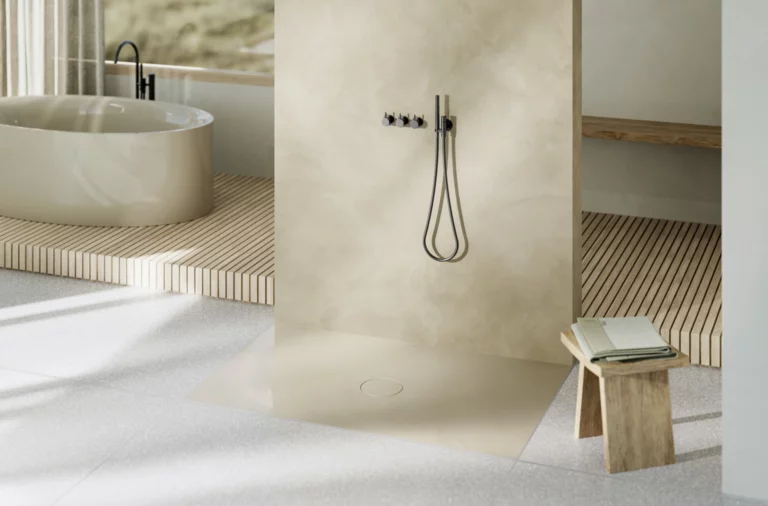 Salle de bains lumineuse avec douche à l’italienne, baignoire autoportante au fond, banc en bois et tabouret avec livre.